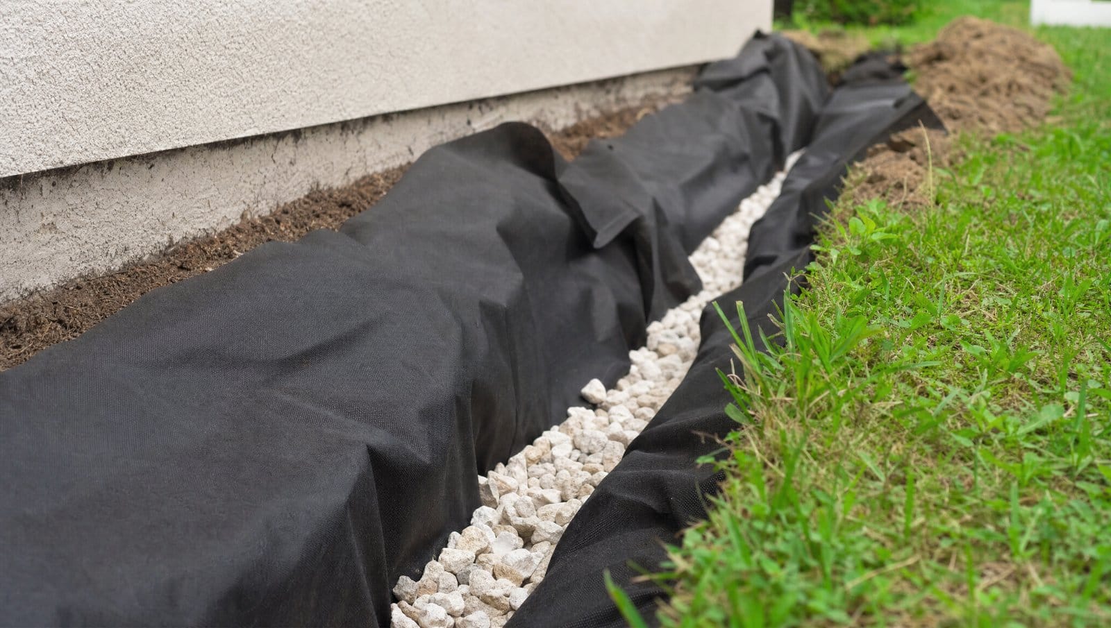 Black geotextile landscape fabric lining a gravel French drain trench in a Florida yard