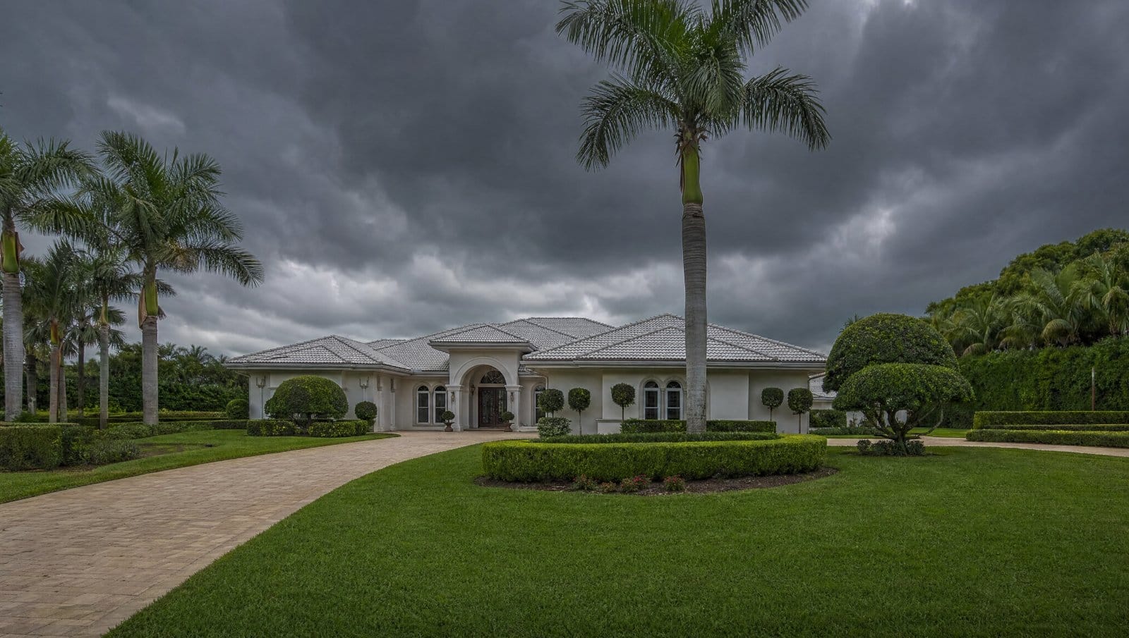 Well-maintained Florida property with freshly trimmed trees under a dramatic stormy sky