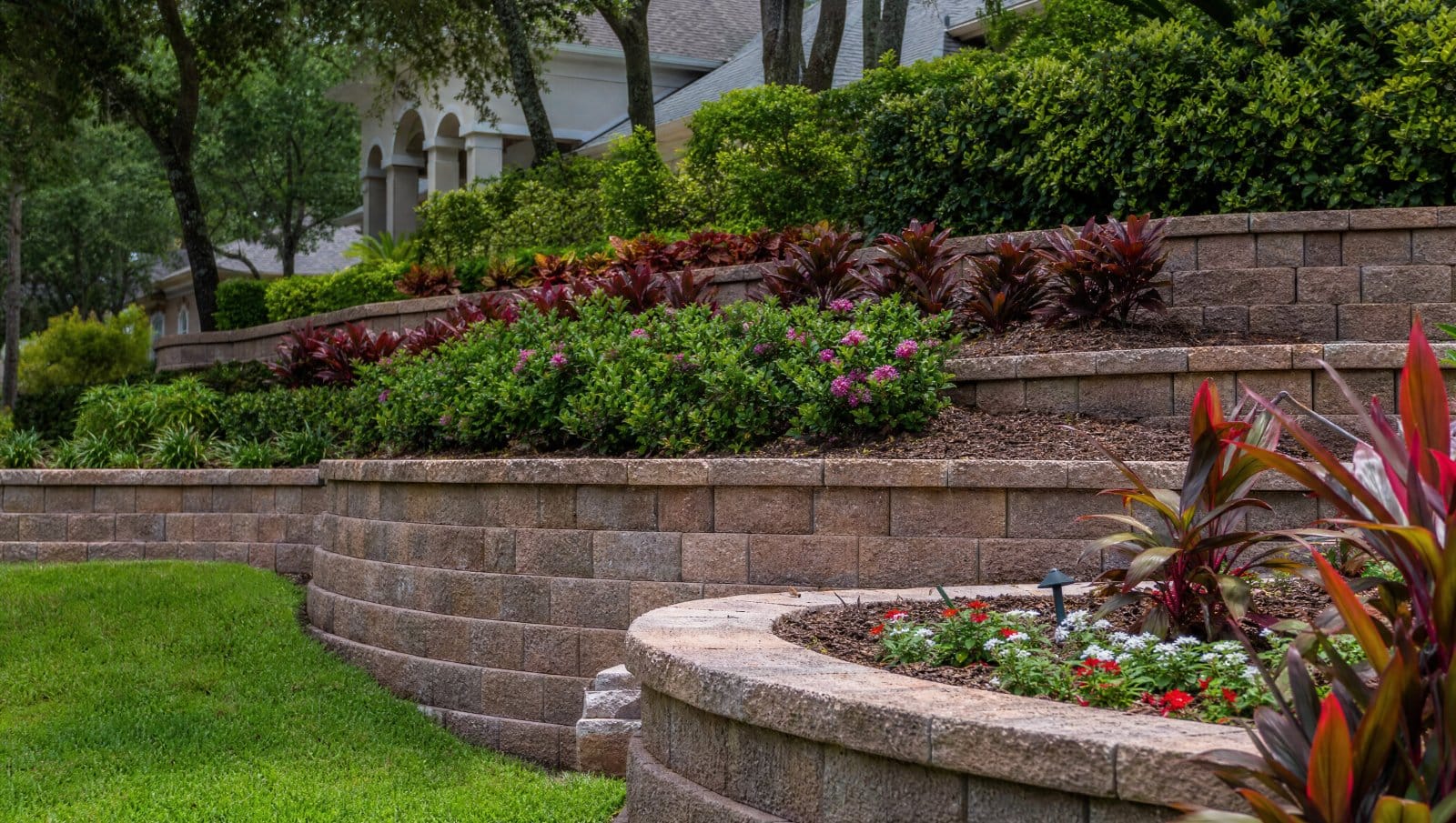 Multi-tiered landscaped retaining wall with colorful plantings on a sloped Central Florida yard
