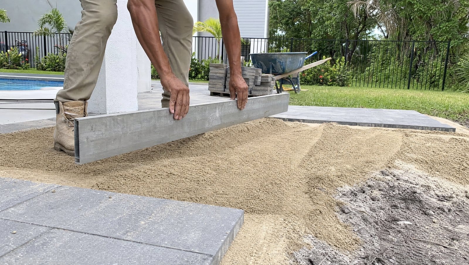 Pavers being leveled on uneven ground with a screed and sand in a Florida yard