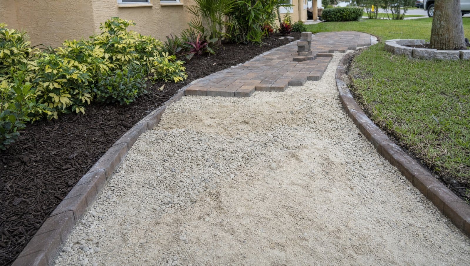 Partially installed paver walkway showing the sand and gravel base layer in a Florida yard