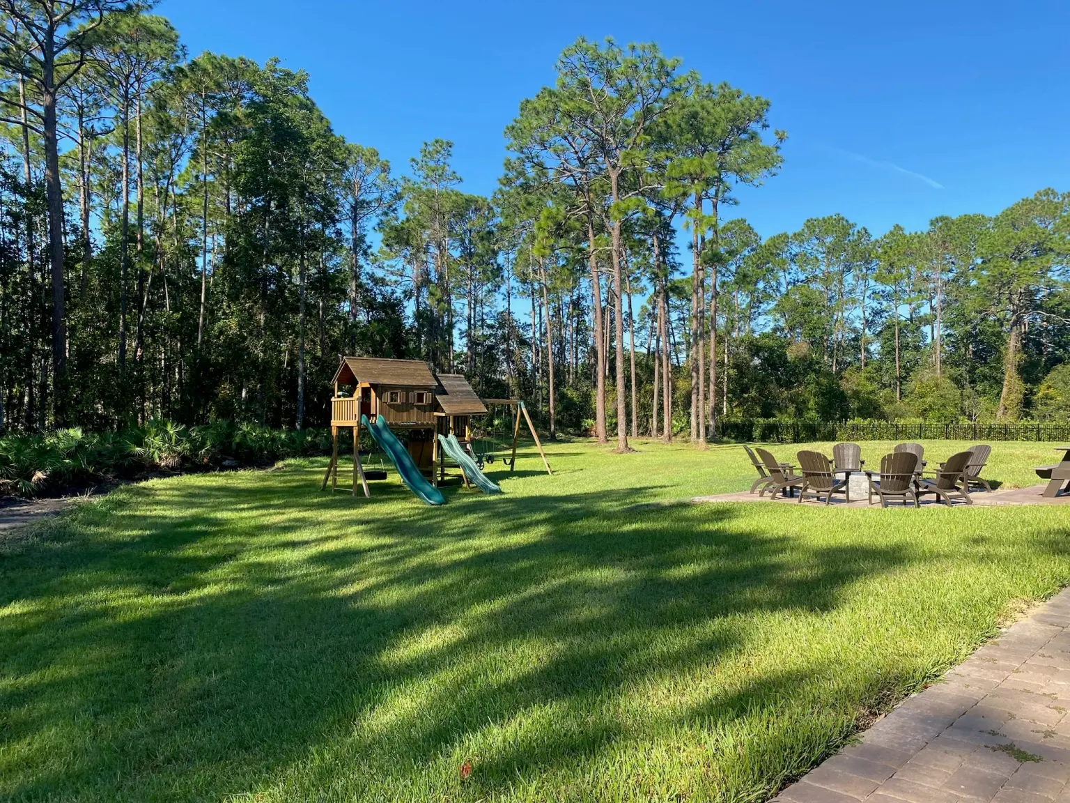Finished backyard with playset and pine treeline after fall landscape cleanup in Central Florida
