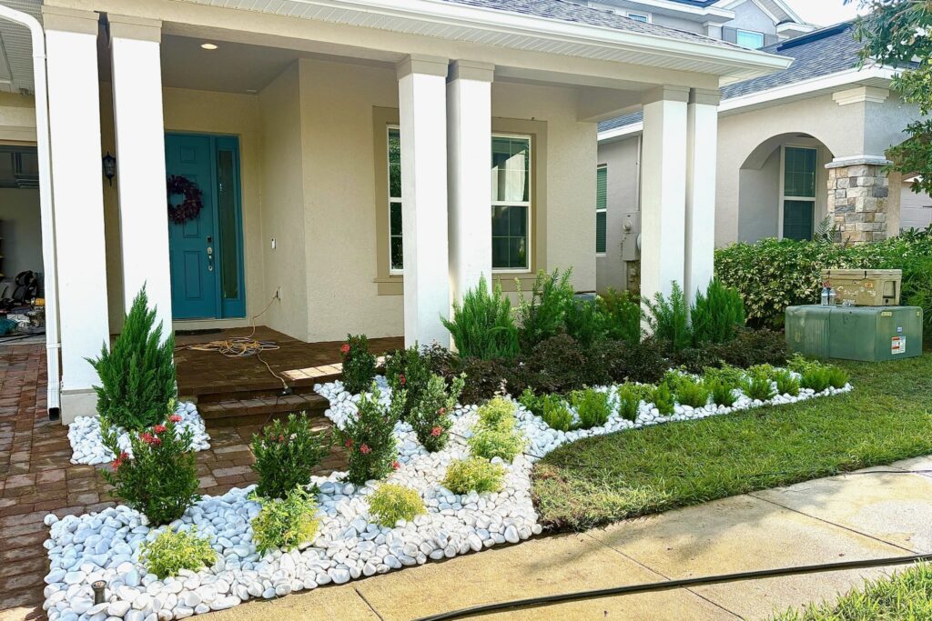 White river rock garden bed with shrubs and junipers framing a home entrance — garden bed installation by DeAngelo's Land Services