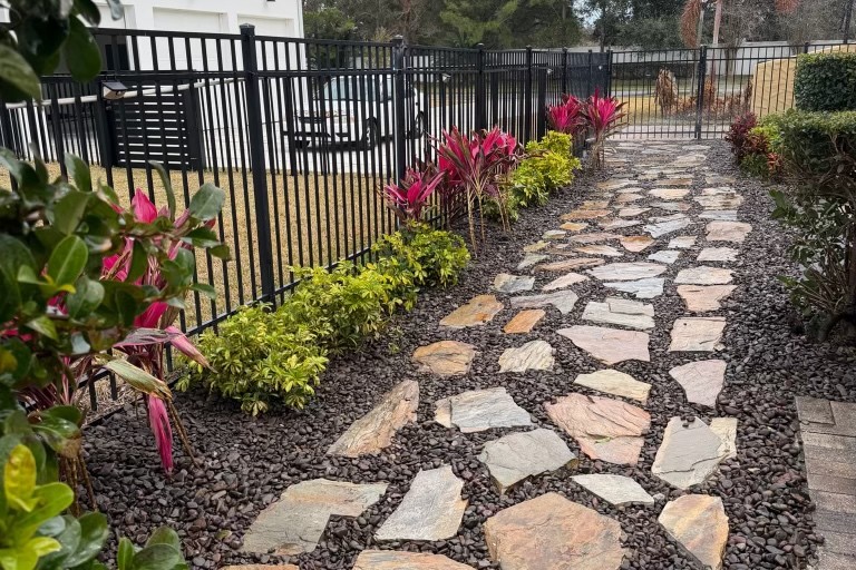 Irregular flagstone walkway with cordyline plantings and black aluminum fence — hardscaping by DeAngelo's Land Services