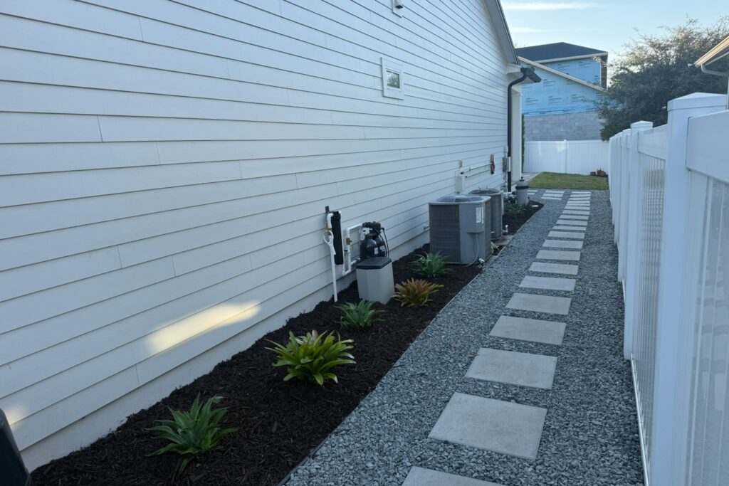 Side-yard gravel drainage channel with paver stepping stones and mulched plant bed installed by DeAngelo's Land Services